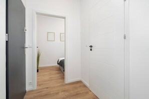 Un pasillo con piso de madera, una cama con cabecera blanca y dos cuadros en la pared.