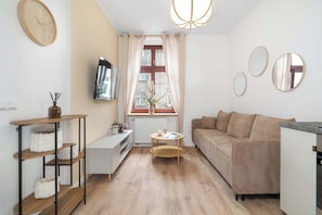 En moderne stue med sofa, sofabord, fjernsyn og et vindue med gardiner.