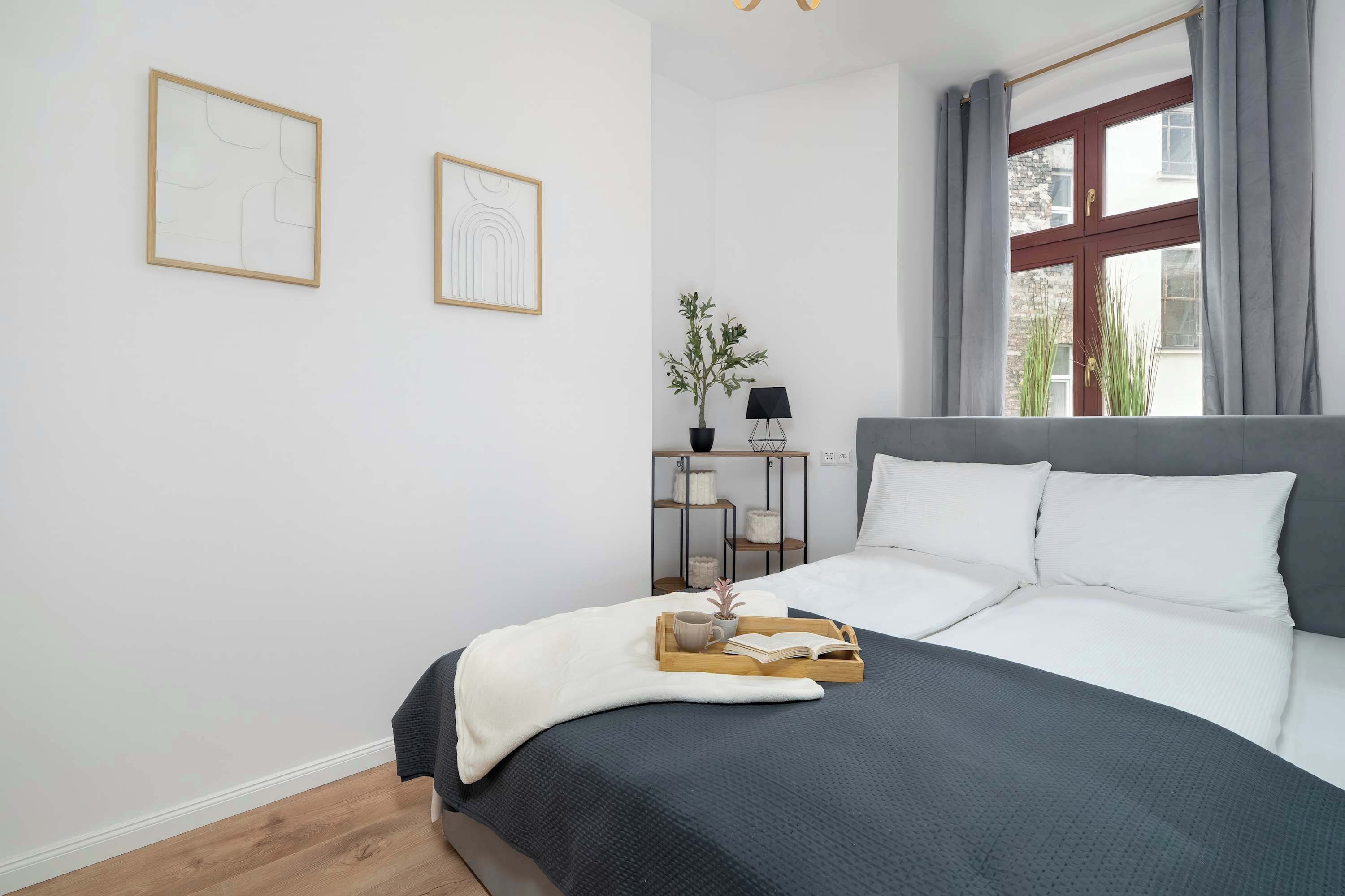 A bedroom with a bed, a bedside table with a lamp, and two framed artworks on the wall.