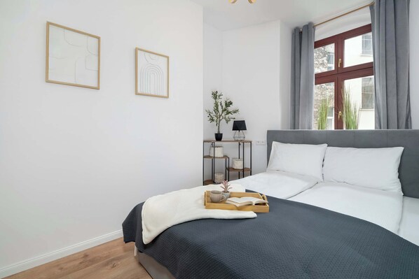 A bedroom with a bed, a bedside table with a lamp, and two framed artworks on the wall. - Cosy Apartments | Near the Market Square (Poznań)