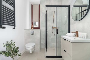 Ein modernes Badezimmer mit Toilette, einer Duschkabine aus Glas, einem Waschbecken mit Pflegeprodukten und einem Spiegel.
