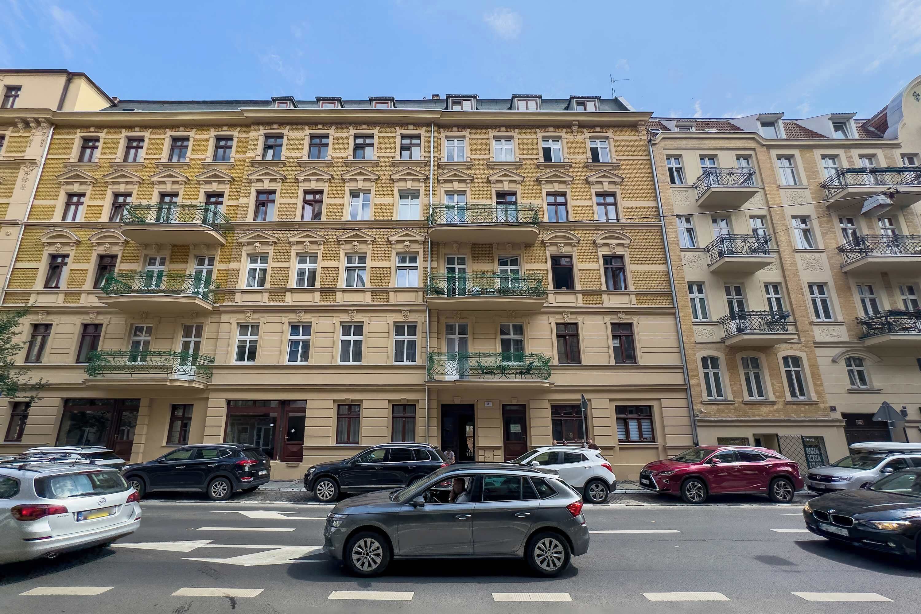 A multi-story building with balconies, parked cars, and a clear sky.