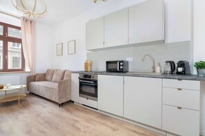 A modern kitchen with white cabinetry, a built-in oven, a microwave, and a coffee machine. - Cosy Apartments | Near the Market Square (Poznań)