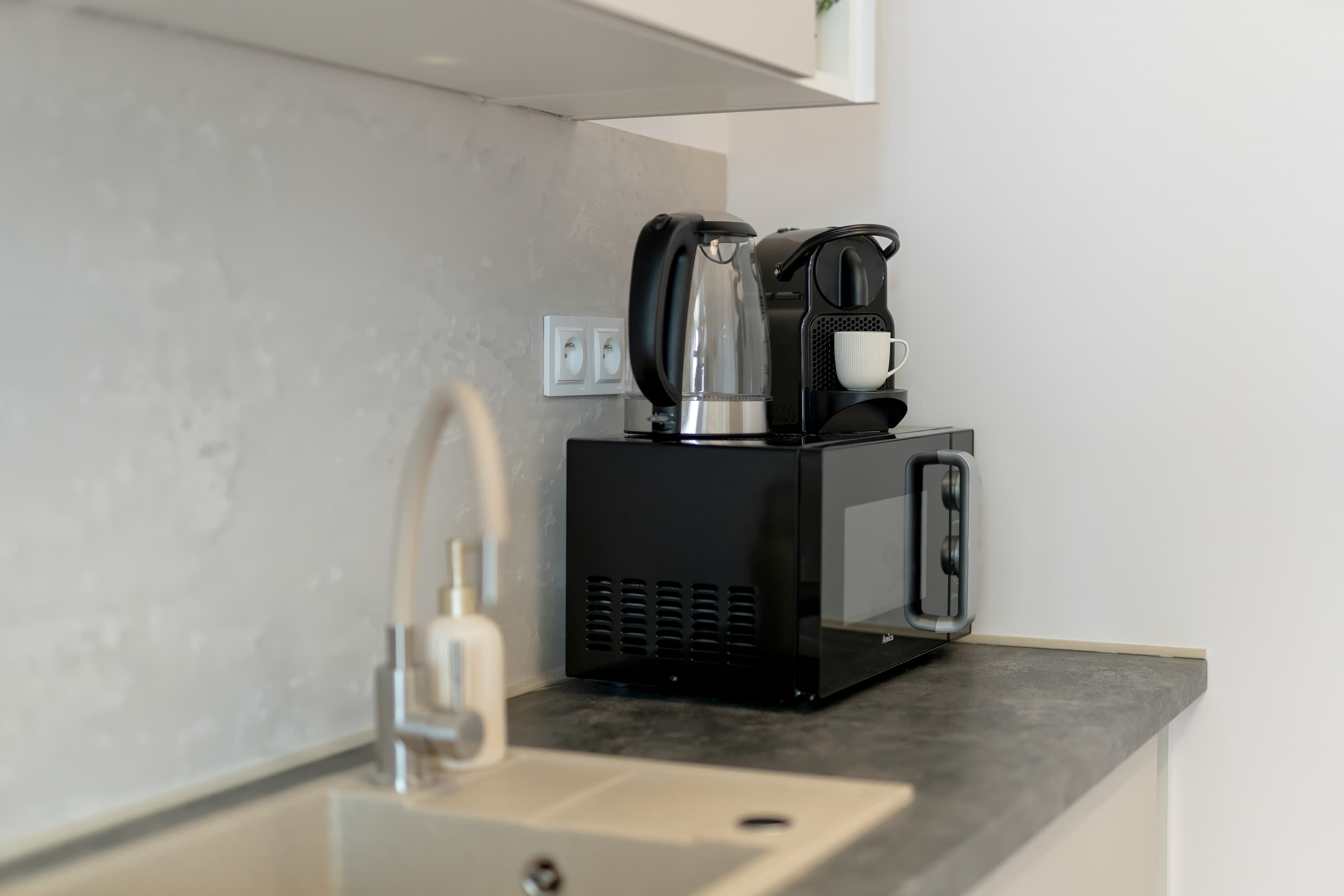 A kitchen with a coffee maker, a microwave, and a sink.