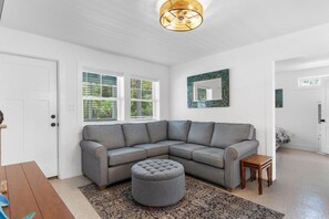 A modern living room with a sectional sofa, ottoman, and a patterned rug. - Turtle Egg Coastal Retreat (Pawleys Island)