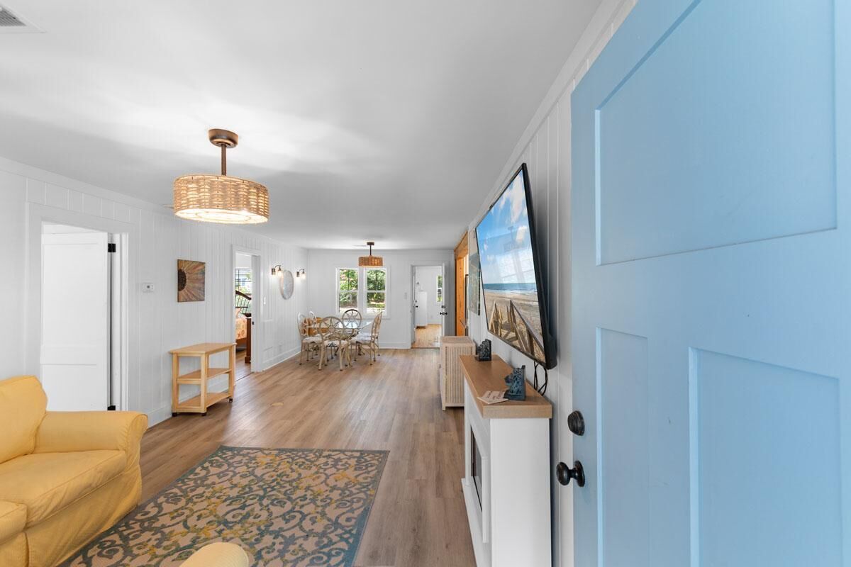 A well-lit hallway with a dining area, a yellow sofa, and a television mounted on the wall.
