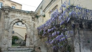 An old stone archway leading to a staircase, with purple wisteria vines climbing over a wall. - "Casa Mura di Pietra" Townhouse, Modica's Historic City Center (Modica)