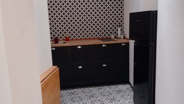 A narrow kitchen with patterned floor tiles, a black refrigerator, and wooden cabinets. - "Casa Mura di Pietra" Townhouse, Modica's Historic City Center (Modica)
