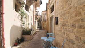 A narrow alley with stone buildings, a small table with a chair, and potted plants. - "Casa Mura di Pietra" Townhouse, Modica's Historic City Center (Modica)