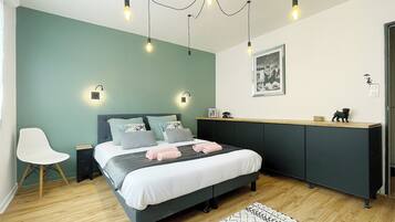 A modern bedroom with a bed, bedside tables, a chair, a desk, and a hanging light fixture.