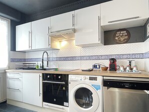 Una cuina moderna amb armaris blancs, forn integrat, rentaplats i rentadora.