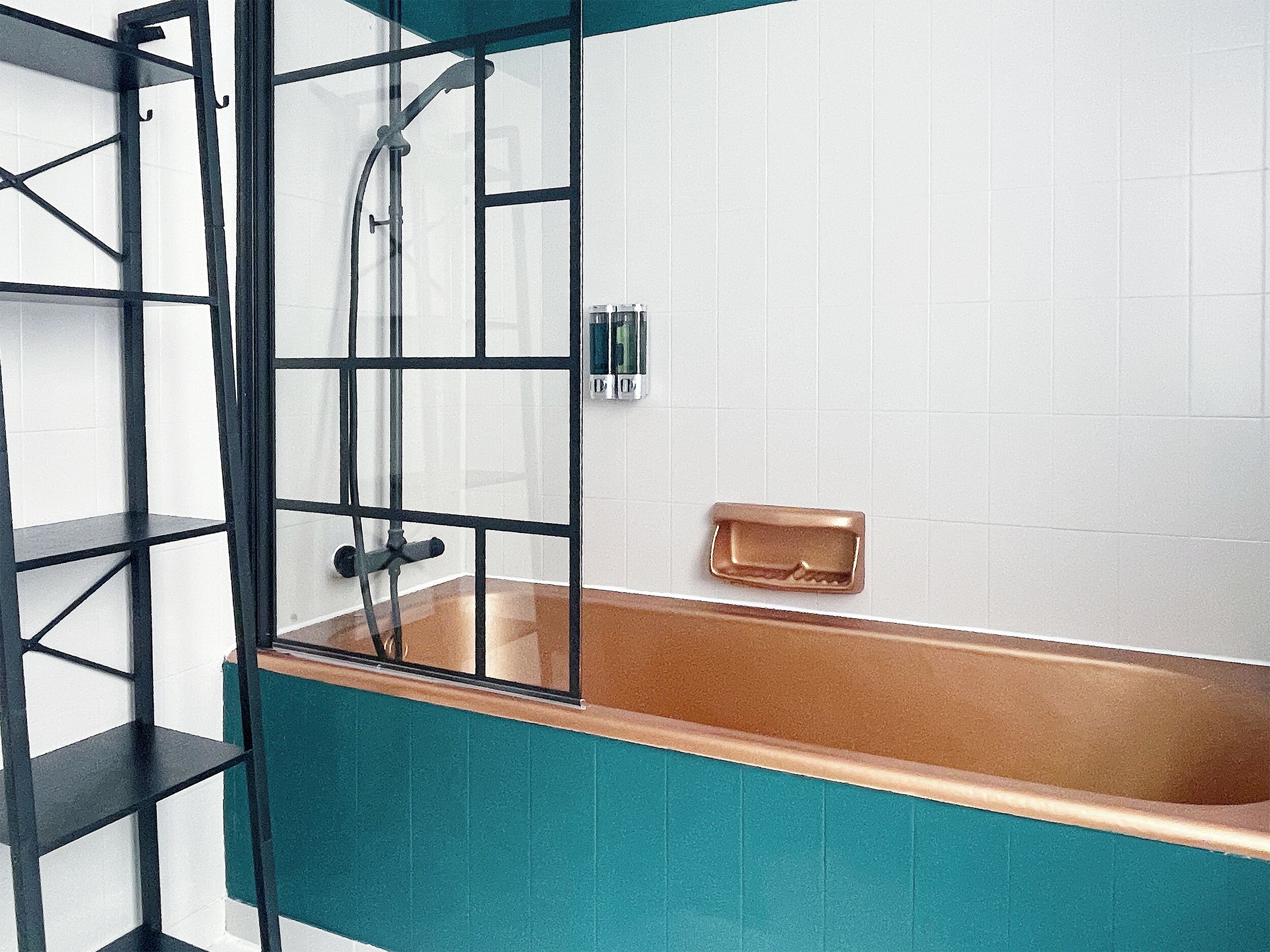 A bathroom with a glass-enclosed bathtub, a black metal shelf, and white tiled walls.