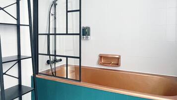 A bathroom with a glass-enclosed bathtub, a black metal shelf, and white tiled walls.