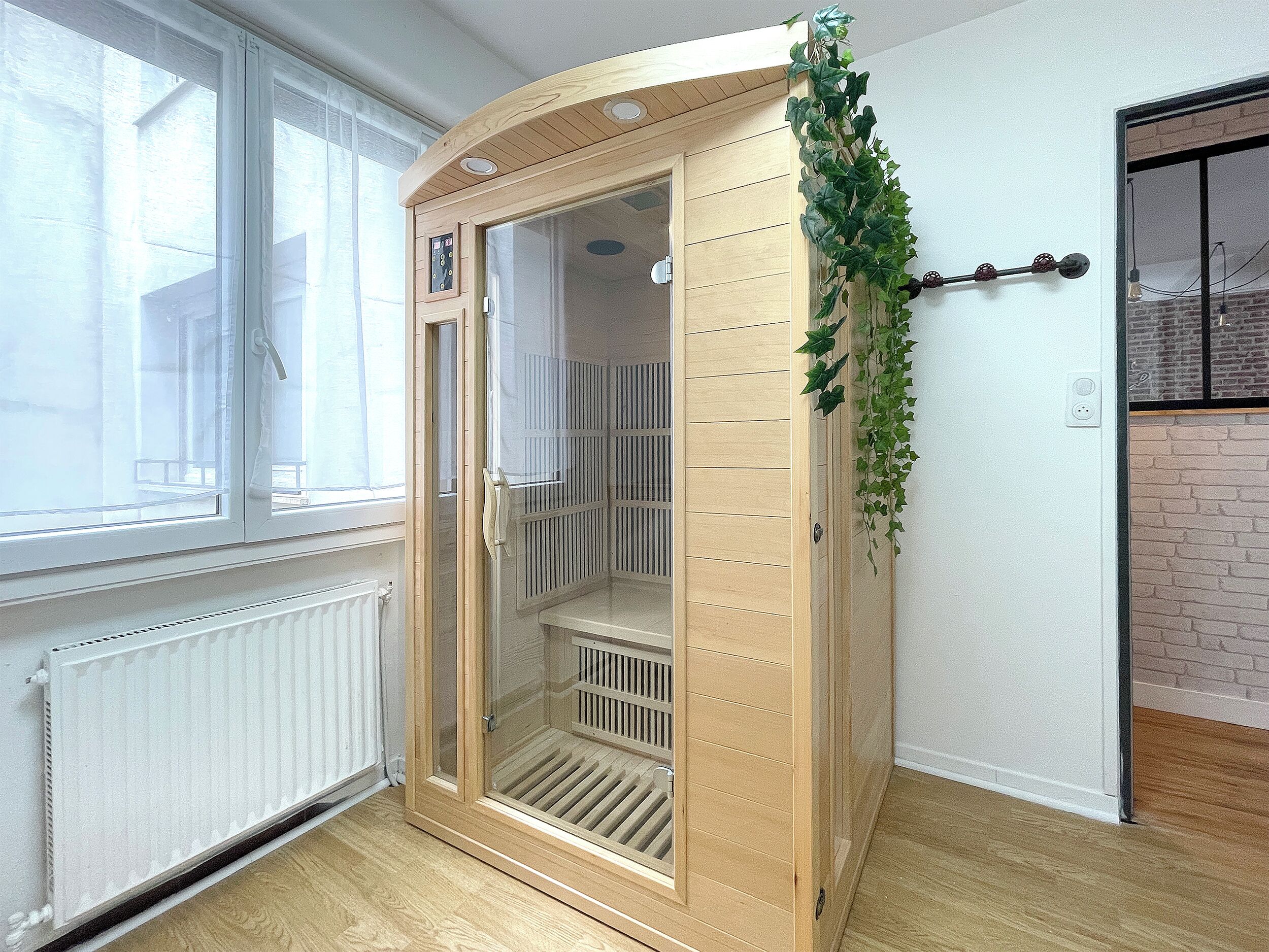 A room with a wooden door, a radiator, a window, and a brick wall.