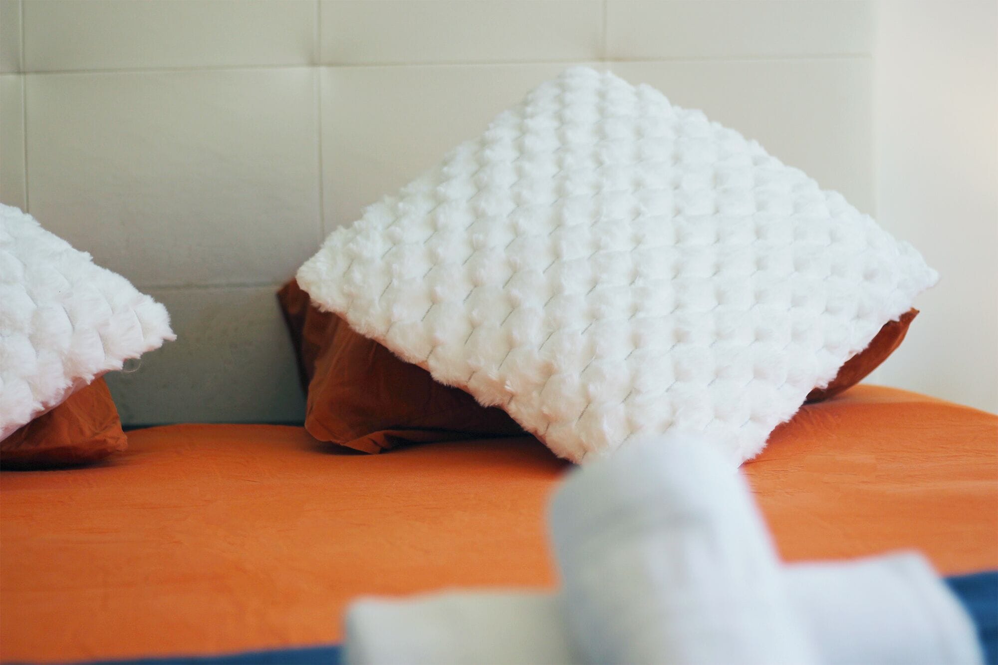 Ein Badezimmer mit einer weißen, strukturierten Duschmatte und einer braunen Badematte auf einem orangefarbenen Boden.