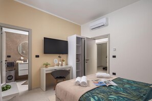 A modern hotel room with a bed, a desk, a chair, a TV, and an air conditioning unit. - Villa Peliceti With Grand Pool (Marcana)