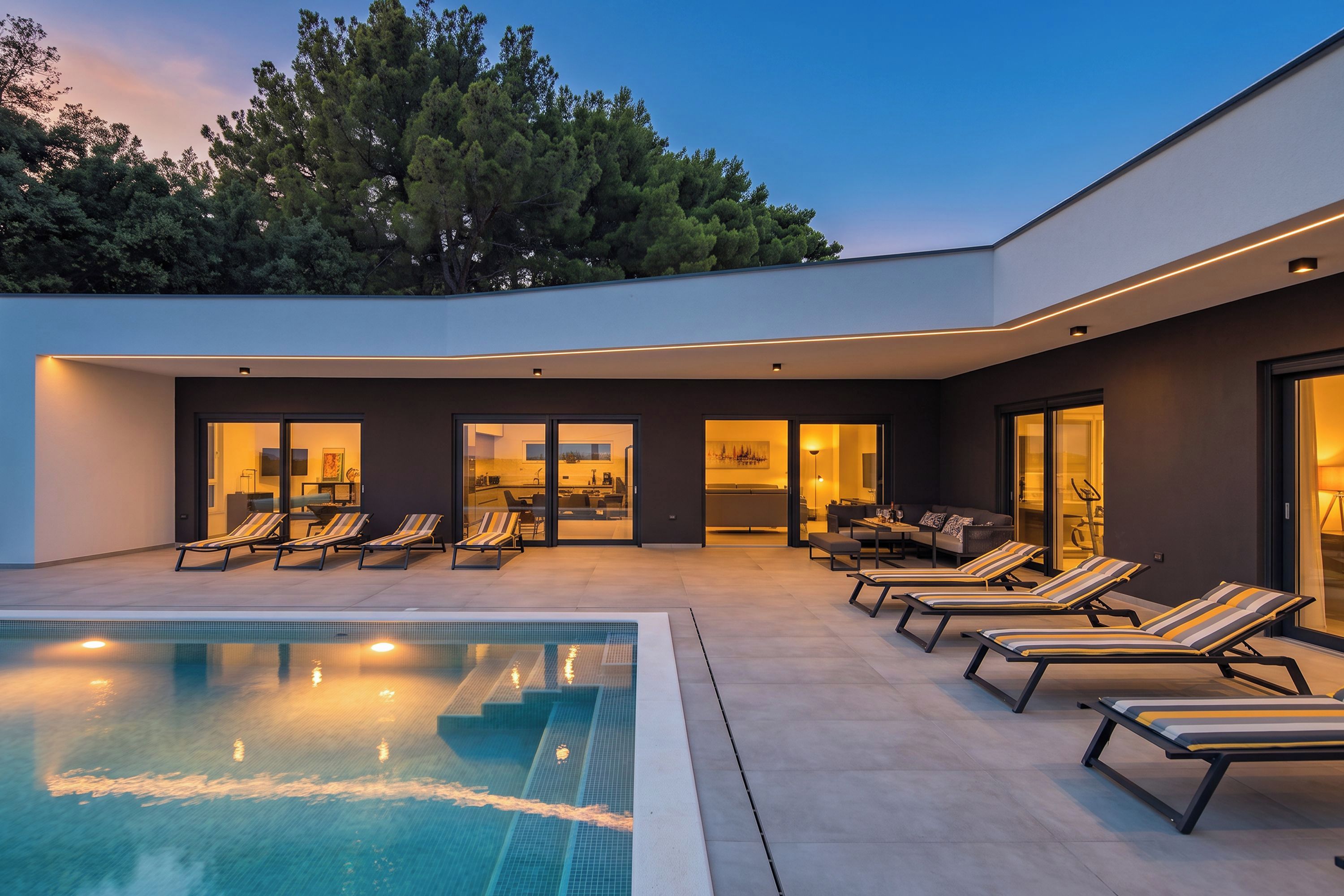 A modern outdoor pool area with lounge chairs and a glass-enclosed kitchen.