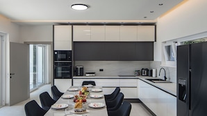 A modern kitchen with a dining area, equipped with appliances and a table set for a meal. - Villa Peliceti With Grand Pool (Marcana)