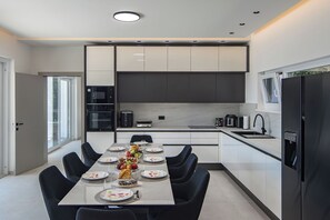 A modern kitchen with a dining area, equipped with appliances and a table set for a meal. - Villa Peliceti With Grand Pool (Marcana)