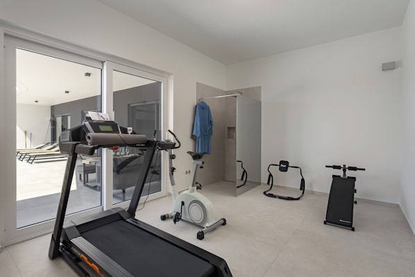 A home gym with a treadmill, an exercise bike, and a stationary bike. - Villa Peliceti With Grand Pool (Marcana)