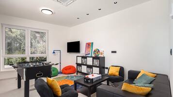 Uma sala de estar moderna com uma mesa de futebol, um sofá com almofadas, uma mesa de centro e uma televisão.