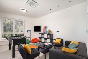 A modern living room with a foosball table, a sofa with cushions, a coffee table, and a television. - Villa Peliceti With Grand Pool (Marcana)