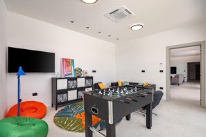 A modern living room with a foosball table, a flat-screen TV, and a sofa. - Villa Peliceti With Grand Pool (Marcana)