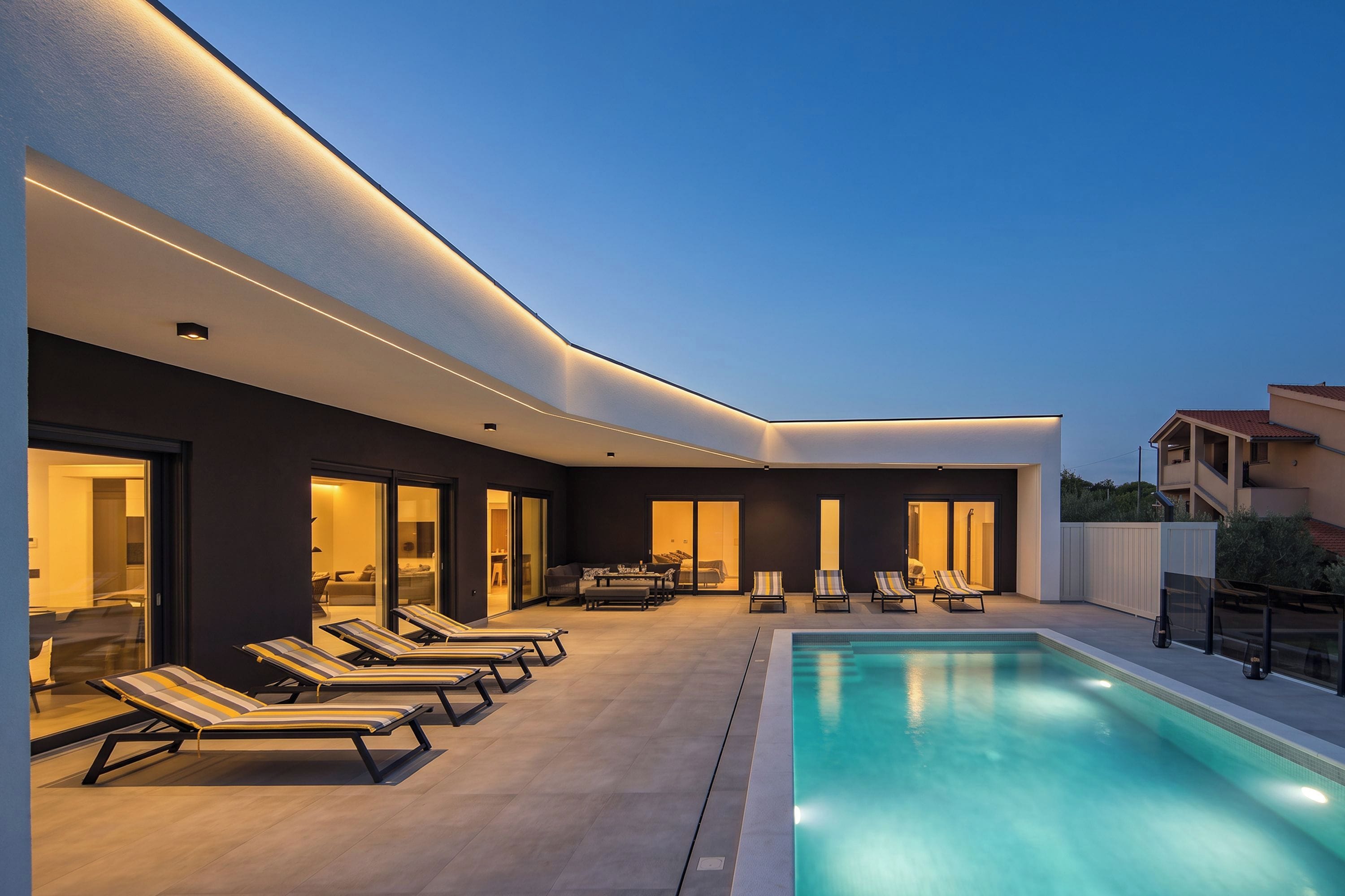 Un área de piscina moderna al aire libre con sillones de descanso y una alberca.