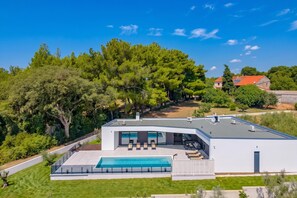 Une maison moderne dotée d’une piscine, de grandes fenêtres et offrant une vue sur les arbres environnants.