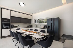 Une cuisine moderne avec un coin repas, comprenant un grand îlot central, des chaises noires et un four encastré.