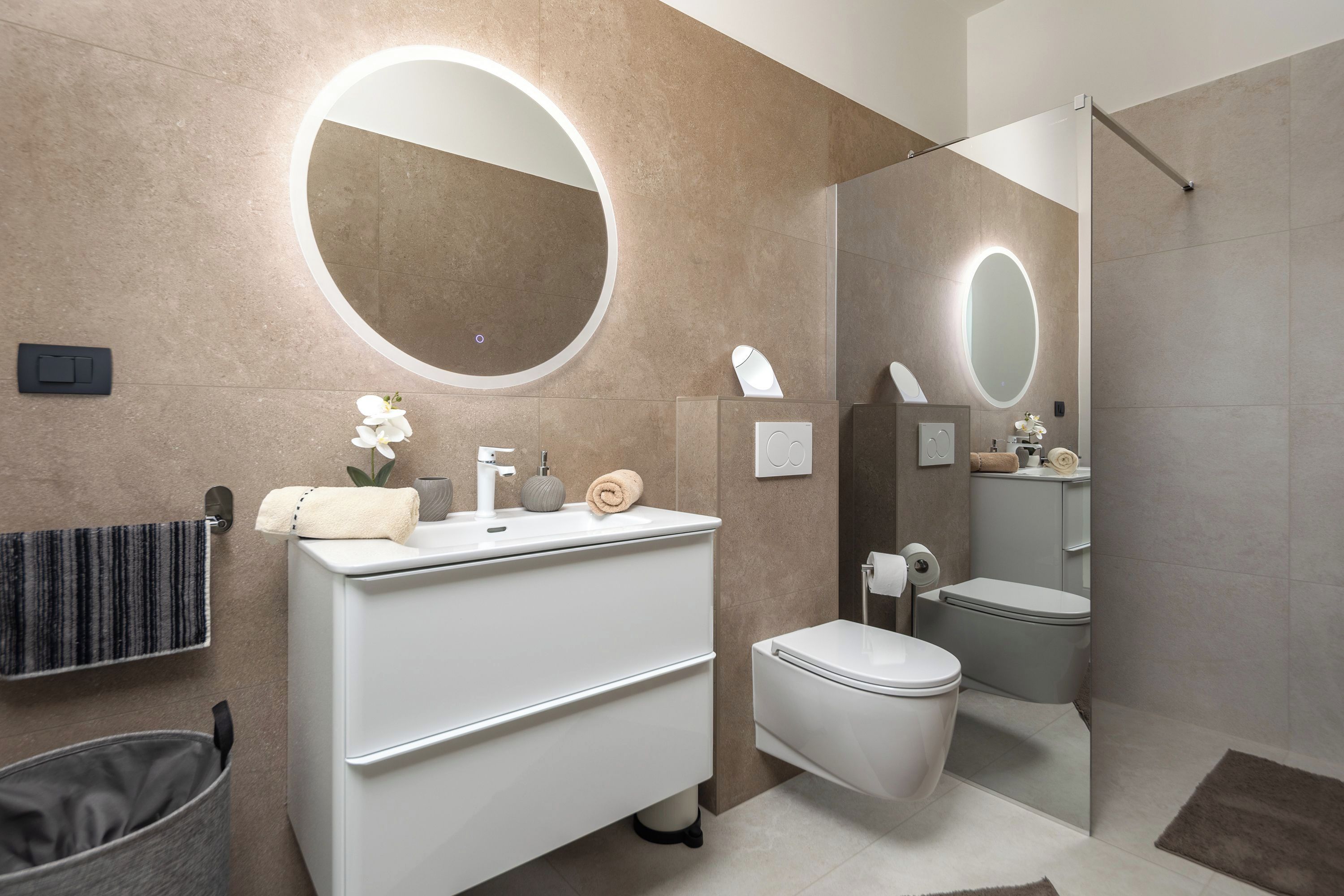 Une salle de bain moderne avec un meuble-lavabo blanc, un miroir rond, des toilettes et un espace douche.