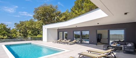 A modern house with a swimming pool, sun loungers, and a patio area.