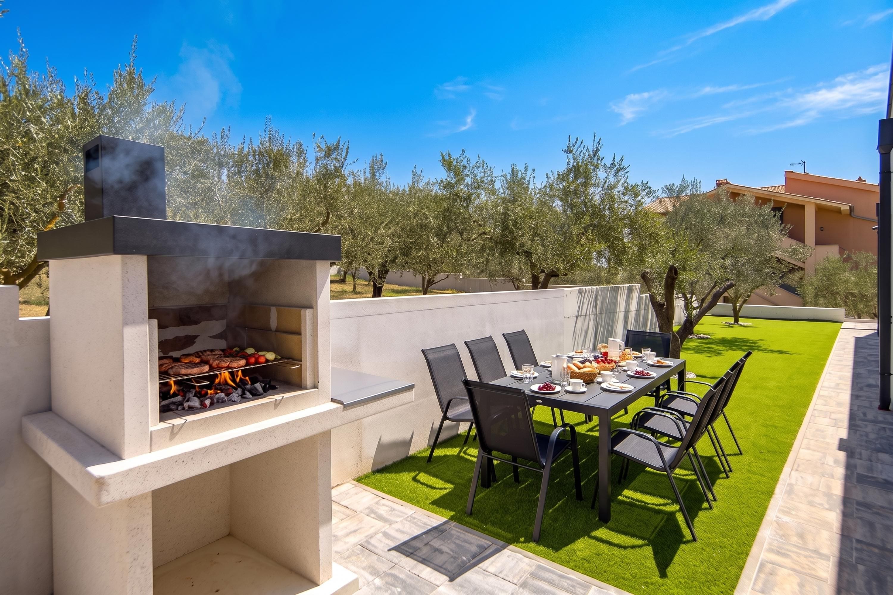 An outdoor patio with a barbecue grill, a dining table with chairs, and a well-maintained lawn.