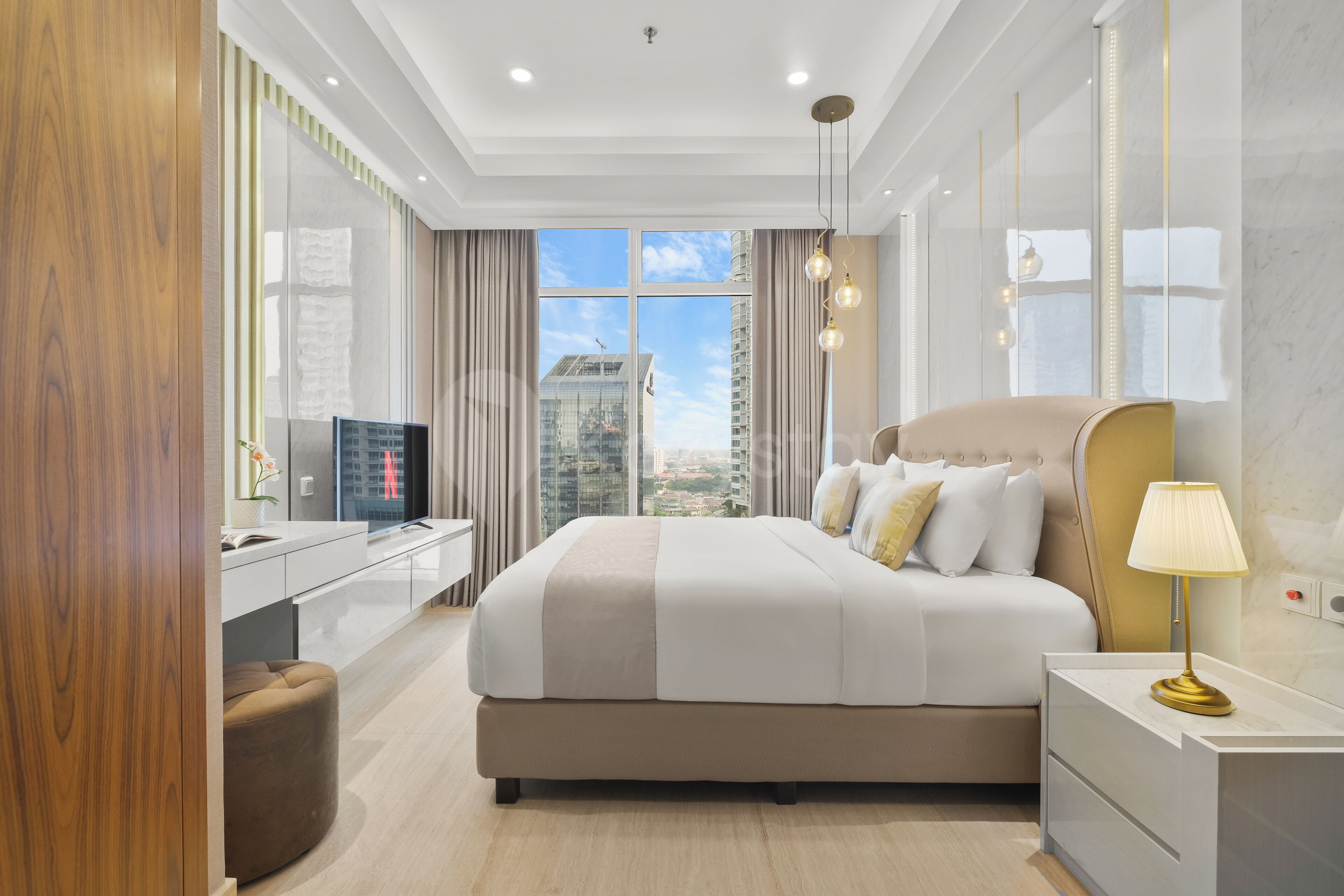 A modern hotel room with a large bed, a desk, a TV, and a view of the cityscape.