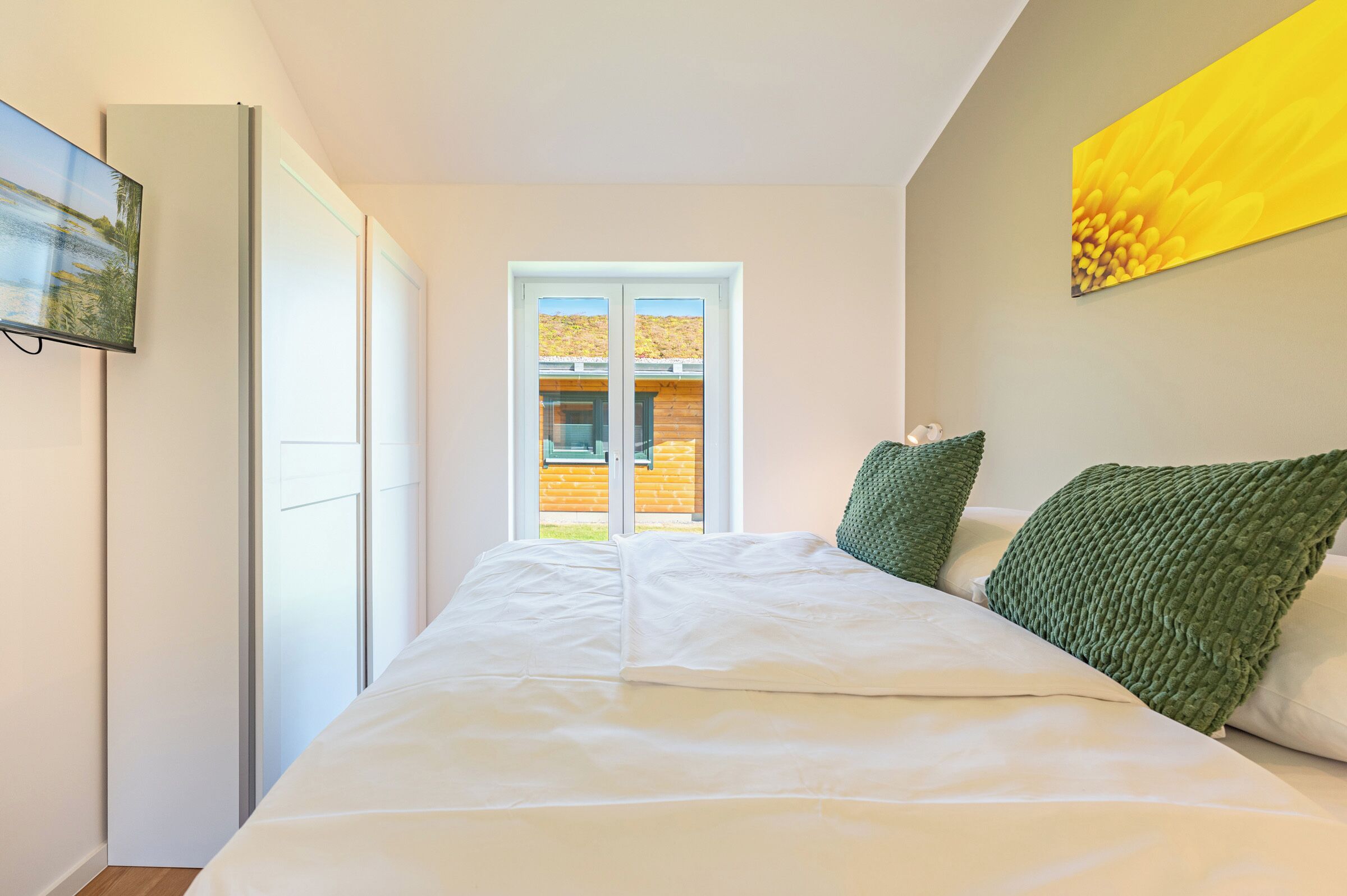 Una camera da letto con un letto, dei cuscini, una finestra e un quadro appeso al muro.
