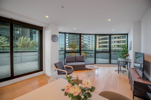 A modern living room with a sofa, armchair, coffee table, and a TV stand. - SkyHome 2BR | Rooftop Pool | Designer Terrace (Box Hill)