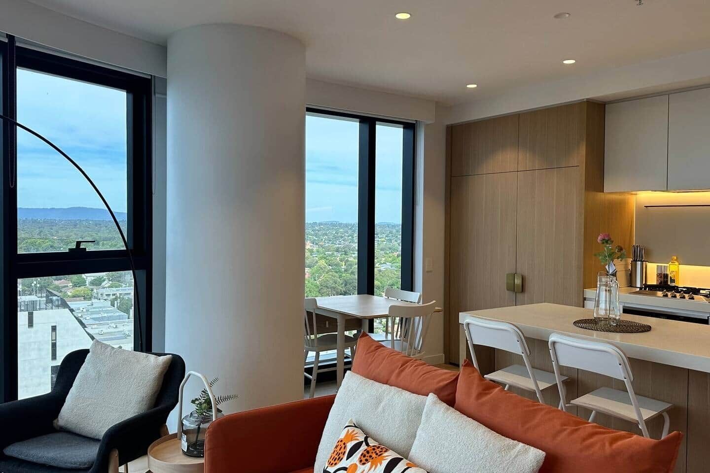 A modern living space with a dining area, kitchen, and large windows offering a city view.