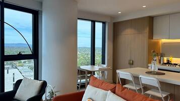 A modern living space with a dining area, kitchen, and large windows offering a city view.