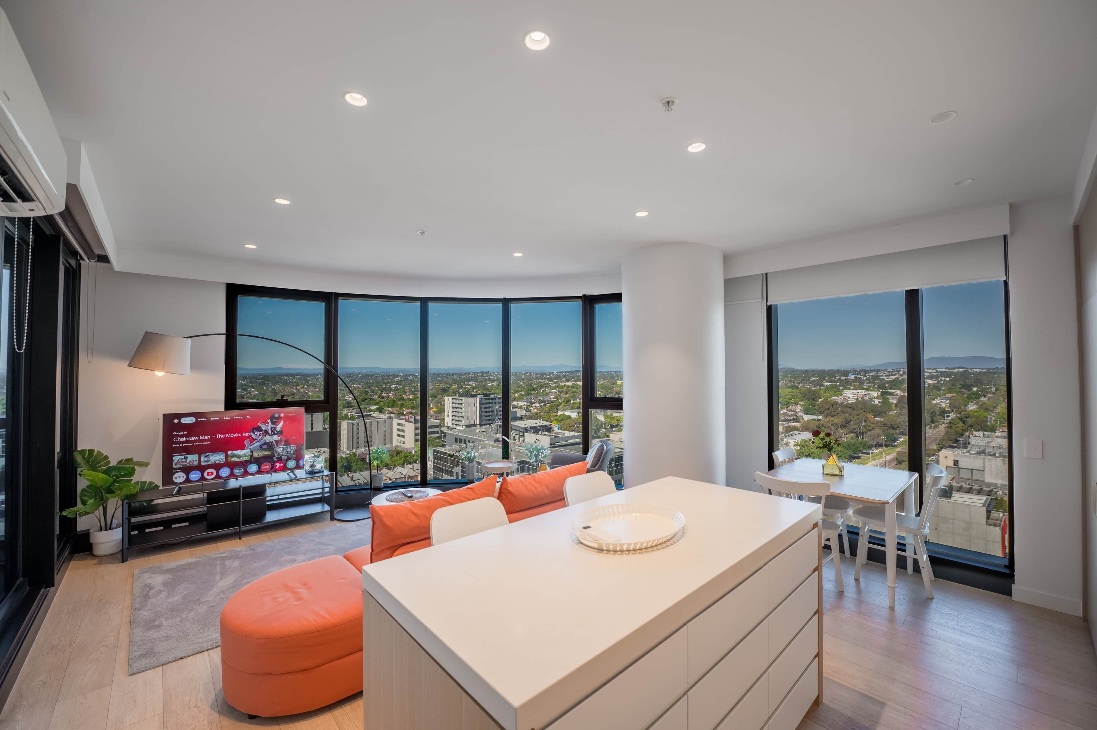 A modern living room with a large window, a flat-screen TV, and a dining area with a view of the city.