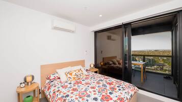 A bedroom with a bed, bedside tables, a nightstand, an air conditioning unit, and a large window with a city view.