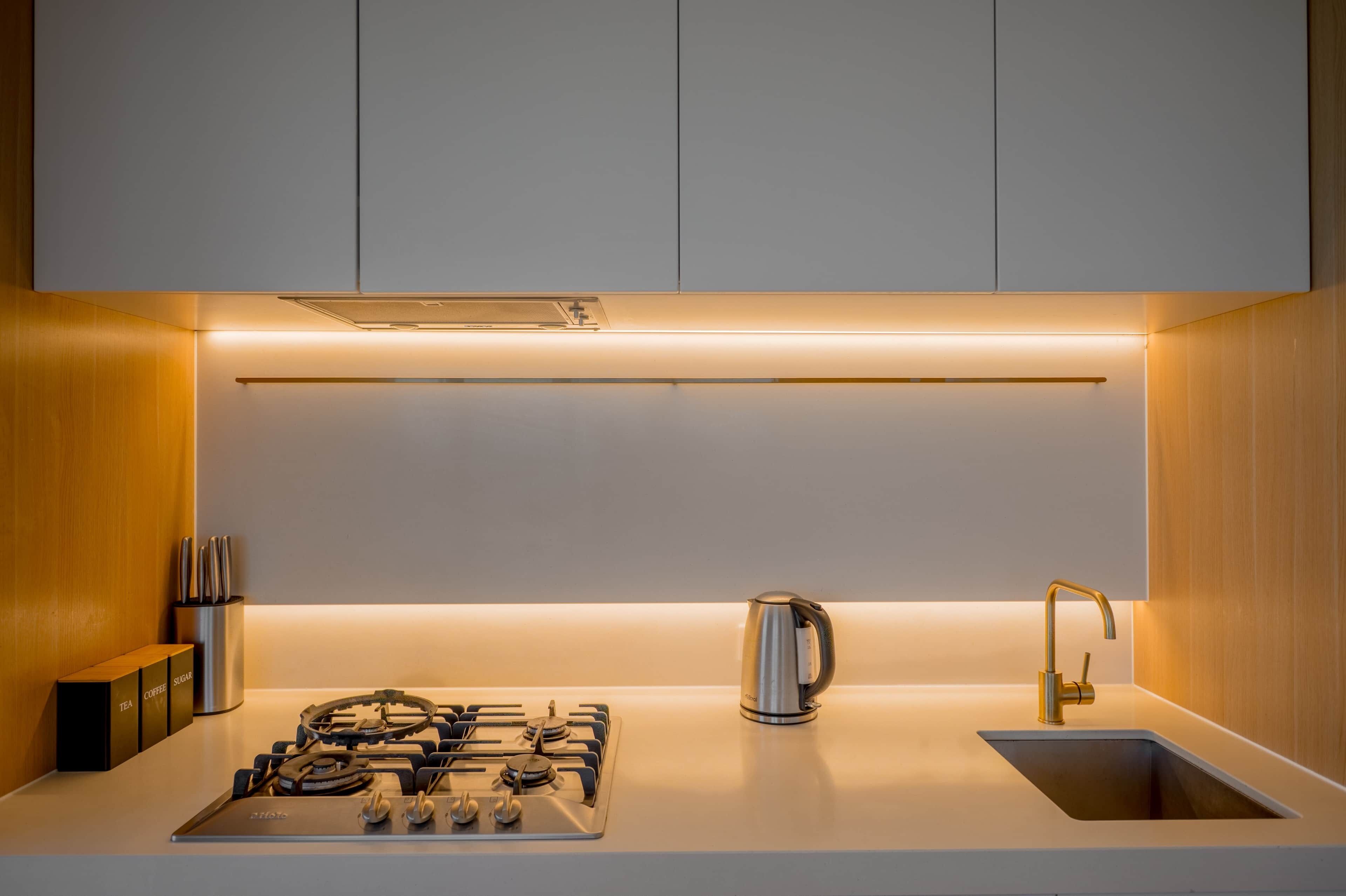 A modern kitchen with a gas stove, a kettle, and a sink.