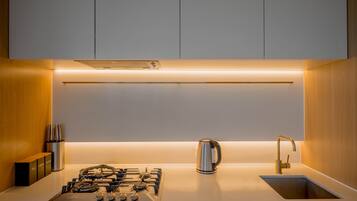 A modern kitchen with a gas stove, a kettle, and a sink.