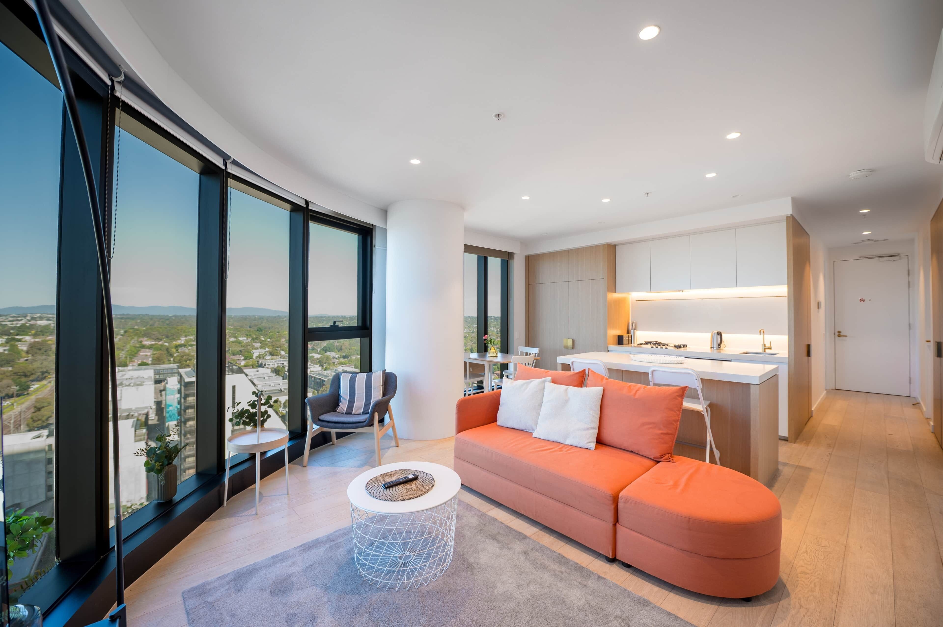 A modern living room with a sofa, a round coffee table, and a view of the city through large windows.