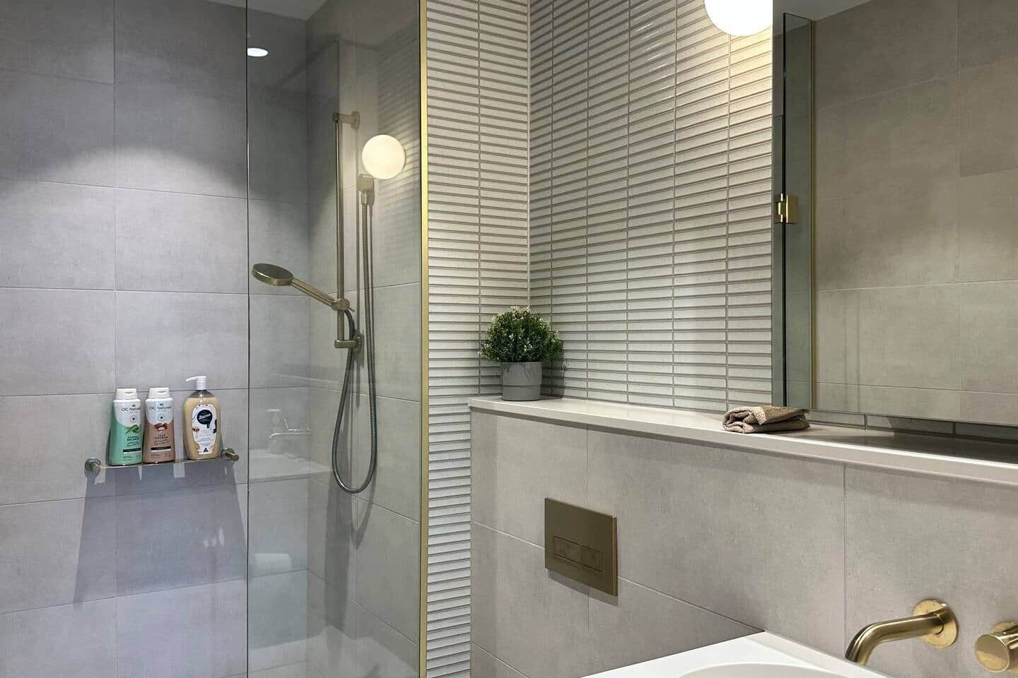 A modern bathroom with a glass-enclosed shower, a vanity with a mirror, and a shelf with toiletries.