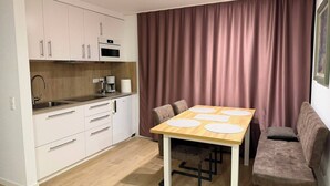 A compact kitchen with white cabinets, a microwave, and a coffee maker. There is a dining table with four chairs and a large window with curtains. - Rebstock Apartment in the wine-growing region of Baden-Baden. (Baden-Baden)