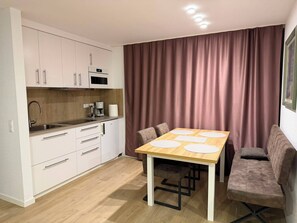 A compact kitchen with white cabinets, a microwave, and a coffee maker. There is a dining table with four chairs and a large window with curtains. - Rebstock Apartment in the wine-growing region of Baden-Baden. (Baden-Baden)