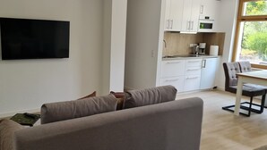 A living room with a flat-screen TV, a sofa, a coffee table, and a view of a kitchen area. - Rebstock Apartment in the wine-growing region of Baden-Baden. (Baden-Baden)