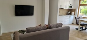 A living room with a flat-screen TV, a sofa, a coffee table, and a view of a kitchen area. - Rebstock Apartment in the wine-growing region of Baden-Baden. (Baden-Baden)