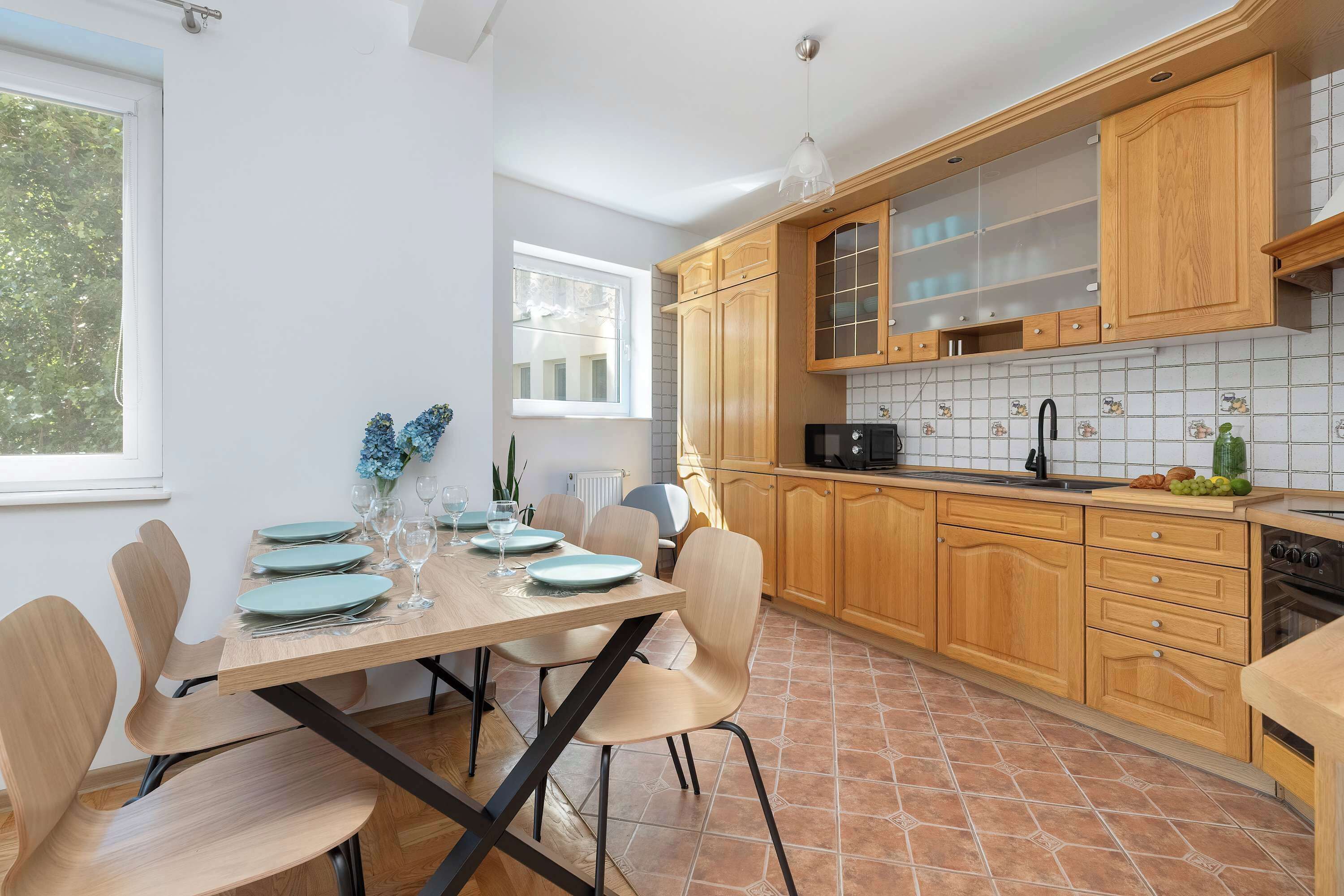 Une cuisine moderne avec des meubles en bois, un pare-feu en carreaux et un coin repas agrémenté d’assiettes et de verres.