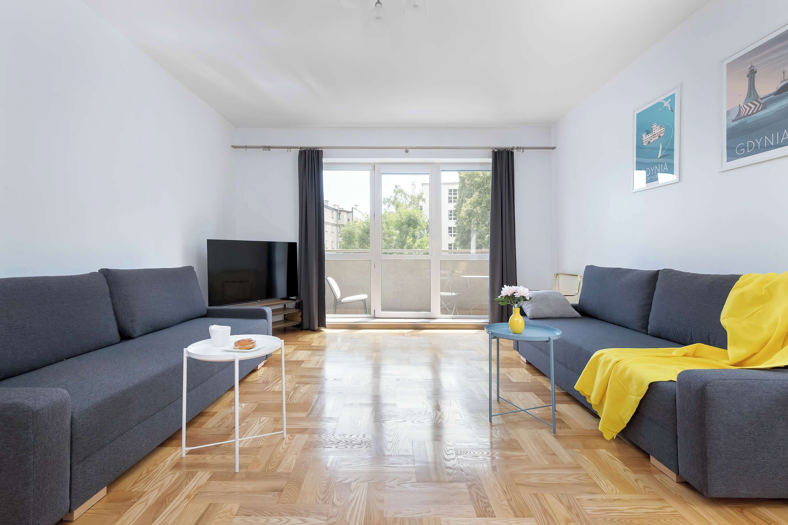 Un salon moderne avec un canapé gris, une petite table blanche et un téléviseur.